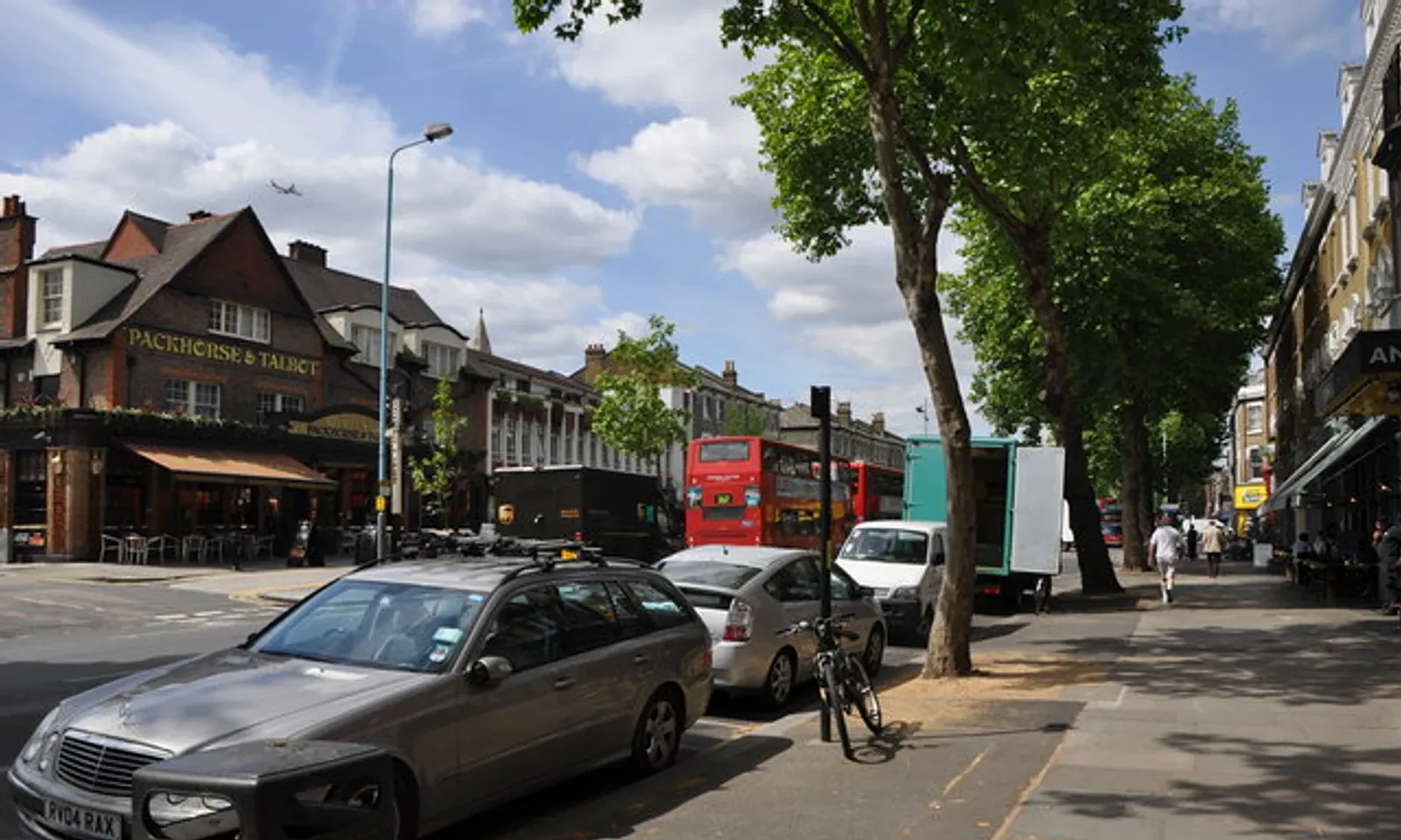 Leafy Chiswick High Road with local shops and a red London bus